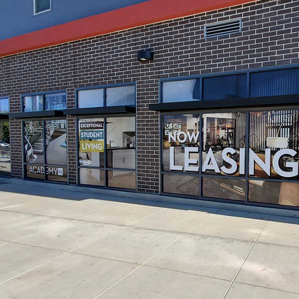 Academy 65 storefront windows with large white NOW LEASING vinyl window graphics